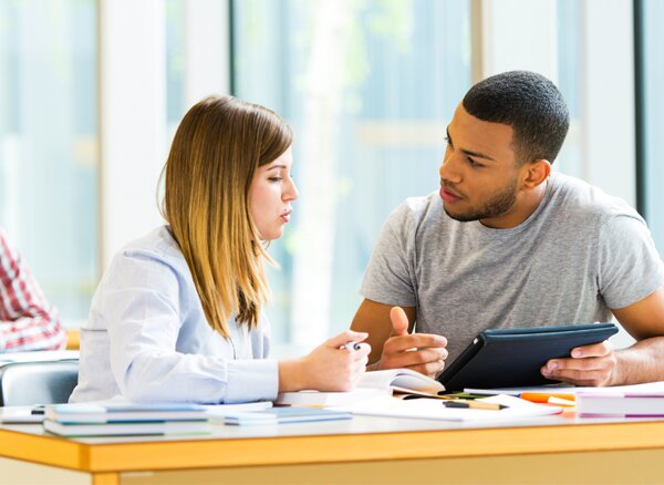 Two young adults studying and conversing in a library.