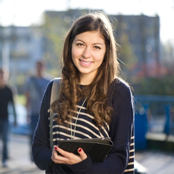 A young female student smiling while holding a binder.