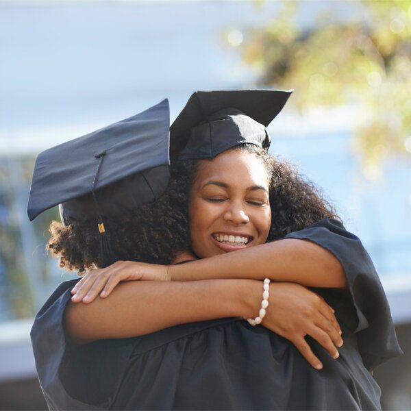 Two students wearing caps and gowns celebrating in an embrace.